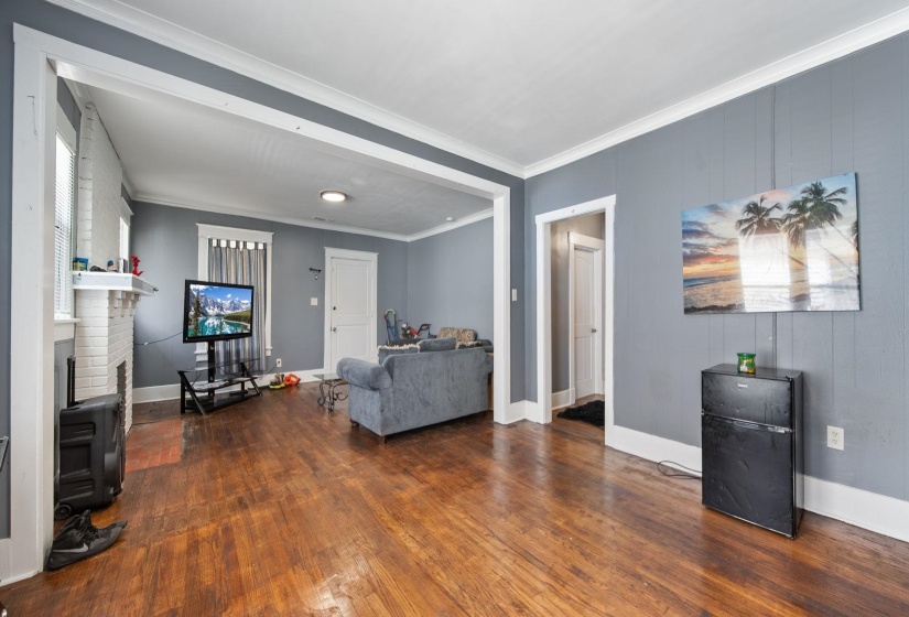 Spacious living area featuring wood-finish flooring, light gray walls, white trim, and a white brick fireplace