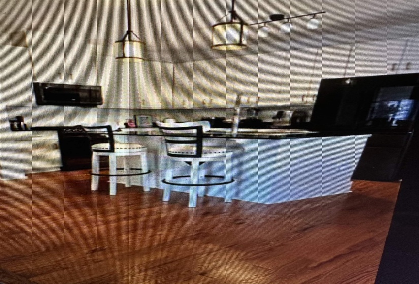 Kitchen featuring wood-finish flooring, white cabinetry, a large center island, pendant lighting, and a built-in microwave