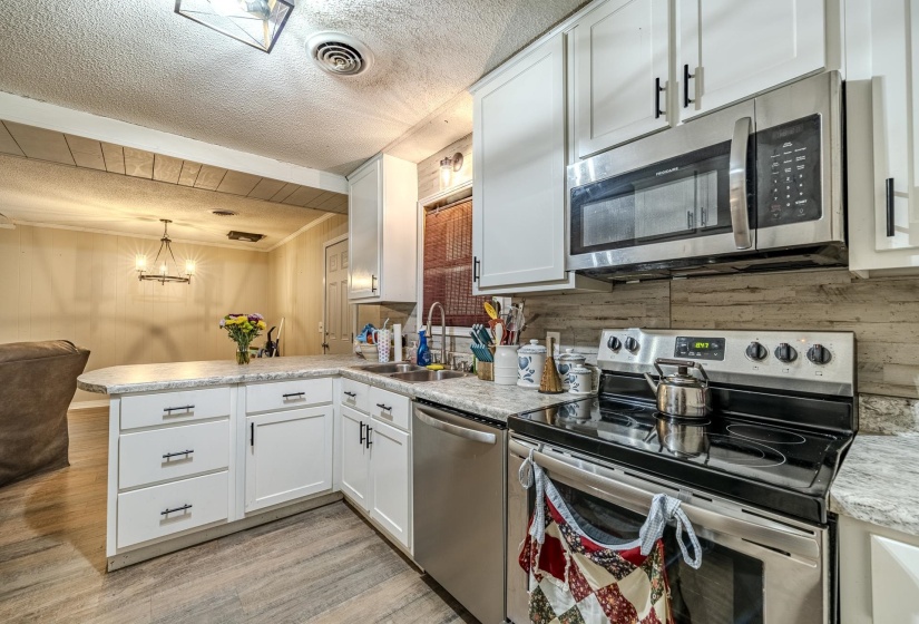 Kitchen featuring white shaker-style cabinetry, stainless steel appliances, wood-finish flooring, light-toned countertops, and a wood-paneled backsplash