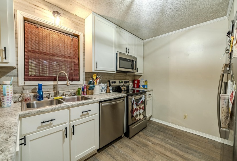 Kitchen featuring white cabinetry with black hardware, stainless steel appliances, a double basin sink with a gooseneck faucet, and wood-finish flooring
