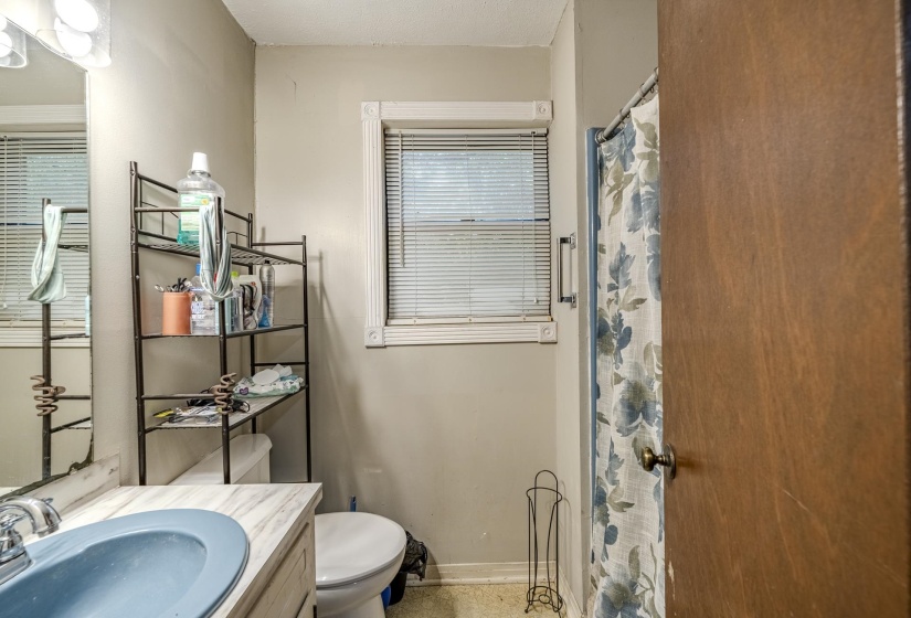 Bathroom featuring a vanity with a light blue basin, a window with blinds, and a shower with a curtain