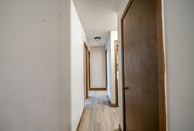 Hallway featuring wood-finish flooring, white walls, and dark wood doors with matching trim