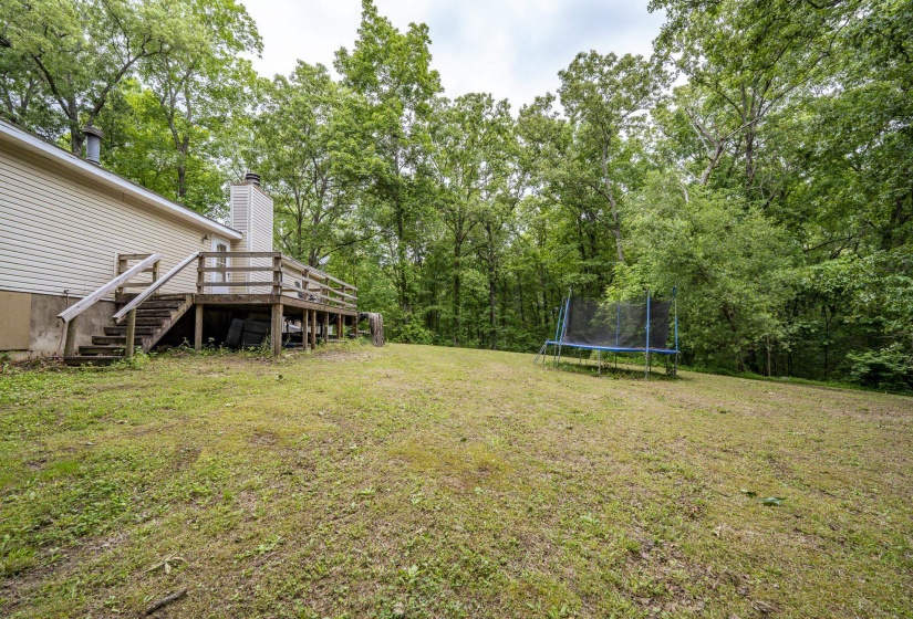Expansive backyard featuring a large wooden deck with railings and stairs, a beige sided exterior, a prominent chimney structure, and a backdrop of mature trees