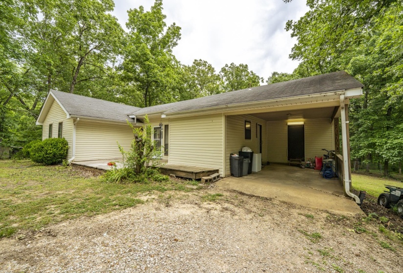 Exterior featuring cream-colored siding, a covered carport, and a gravel driveway