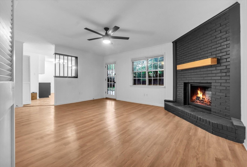 Spacious interior featuring wood-finish flooring, a contemporary ceiling fan, and a painted brick fireplace with a wood mantel