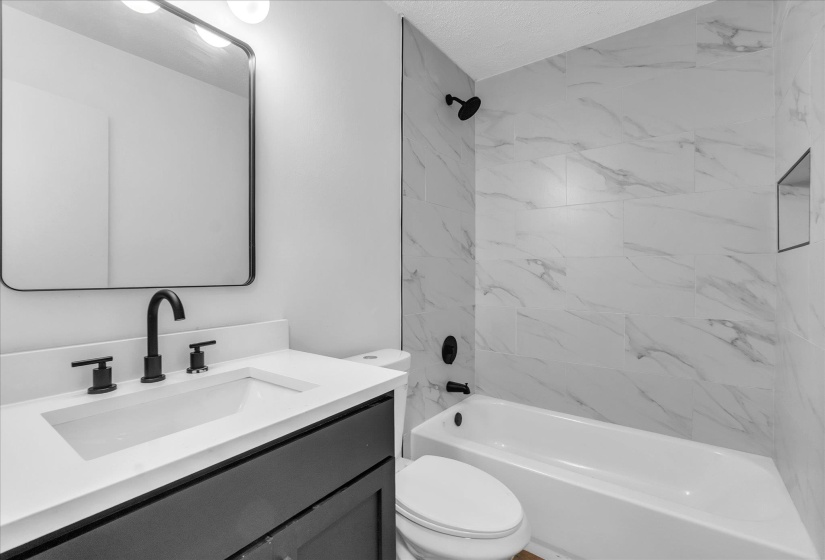 Bathroom featuring a white bathtub with subway tile surround, matte black shower fixtures, a built-in shower niche, and a vanity with a white countertop and matte black faucet
