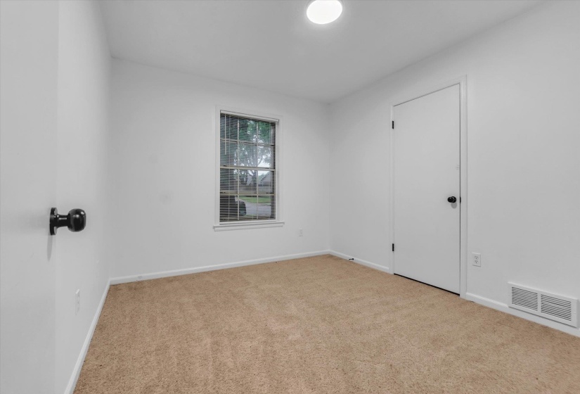 Neutral tone wall paint, carpet flooring, a single window, and a flush-mount ceiling light fixture