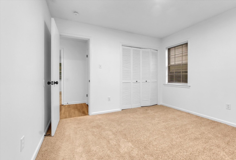 Carpeted room featuring white walls, a single window with blinds, and bi-fold louvered closet doors