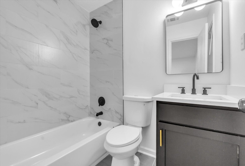 Bathroom featuring a white subway tile shower surround with black fixtures, a white bathtub, and a dark vanity with a white countertop and rectangular mirror