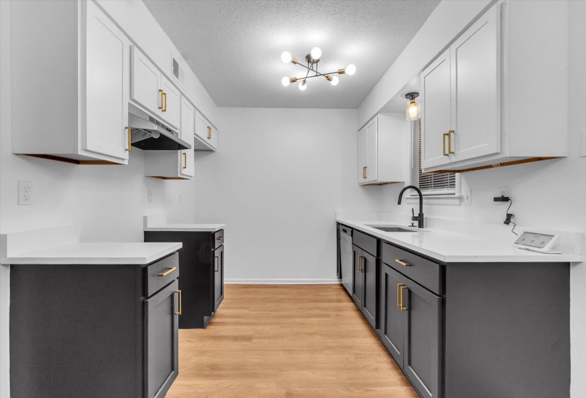 Contemporary kitchen featuring two-tone cabinetry, light countertops, wood-finish flooring, and a modern ceiling light fixture