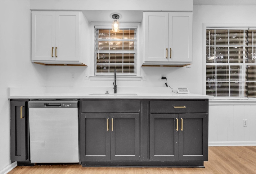 Kitchen featuring two-tone cabinetry with gold-tone hardware, white countertops, stainless steel dishwasher, and a black gooseneck faucet