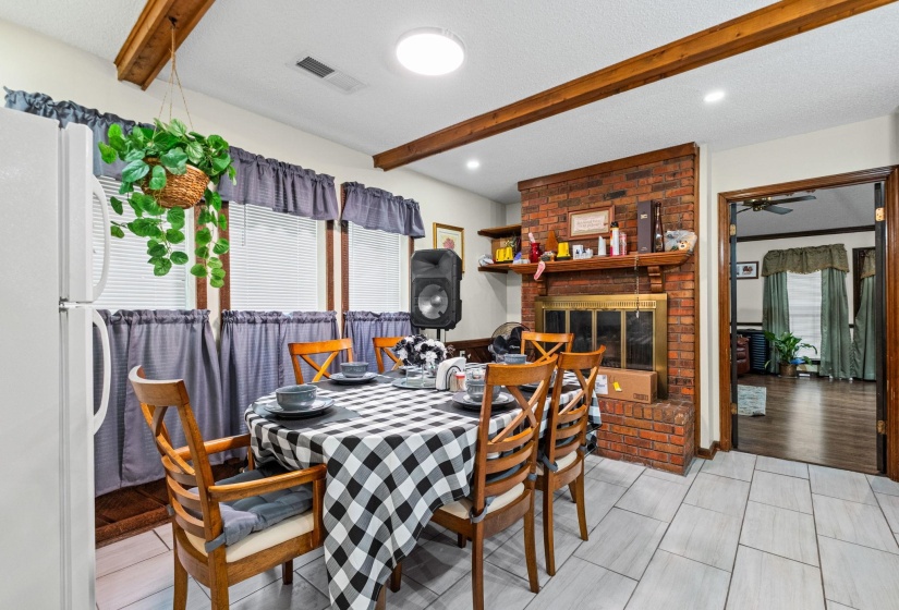 Dining area featuring a brick fireplace with a wood mantle, wood ceiling beams, recessed lighting, and light-toned tile flooring