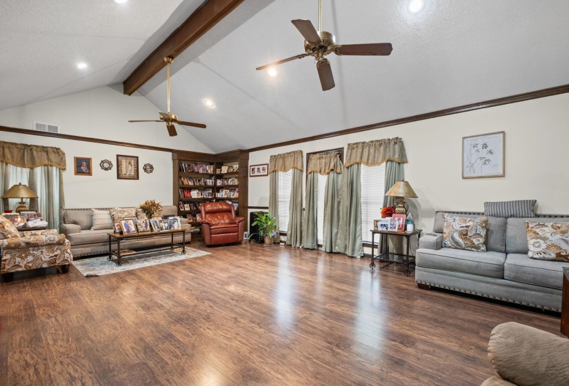 Spacious living area featuring vaulted ceilings with exposed wood beams, wood-finish flooring, two ceiling fans, and built-in corner shelving