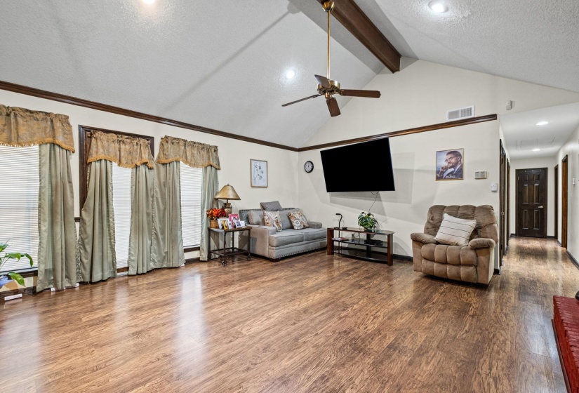 Spacious living area featuring vaulted ceilings with exposed wood beams, wood-finish flooring, and ample natural light from multiple windows
