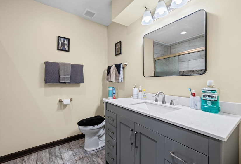 Bathroom featuring a gray vanity with a white countertop and integrated sink, a rectangular mirror, and wood-finish flooring