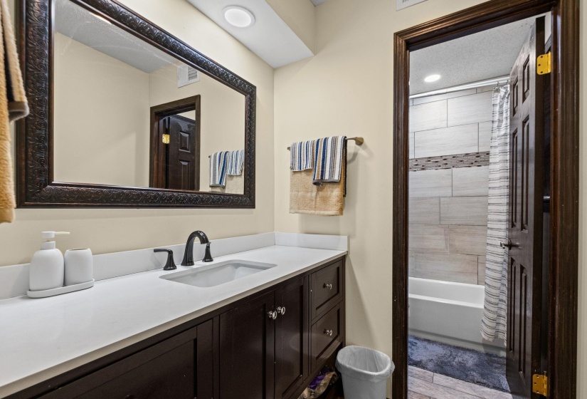 Bathroom vanity featuring a dark wood-finish cabinet, white countertop, and dark-framed mirror