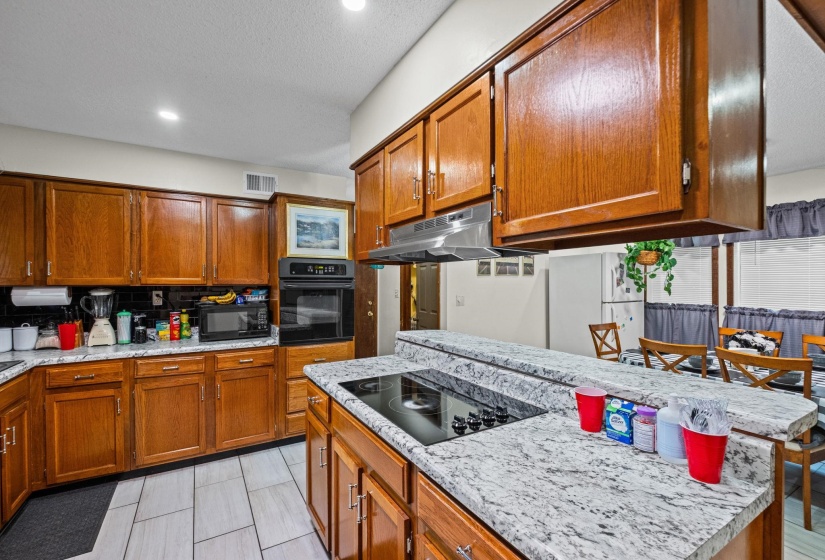 Kitchen featuring wood cabinetry, light-toned countertops, a built-in oven, and a ceramic cooktop