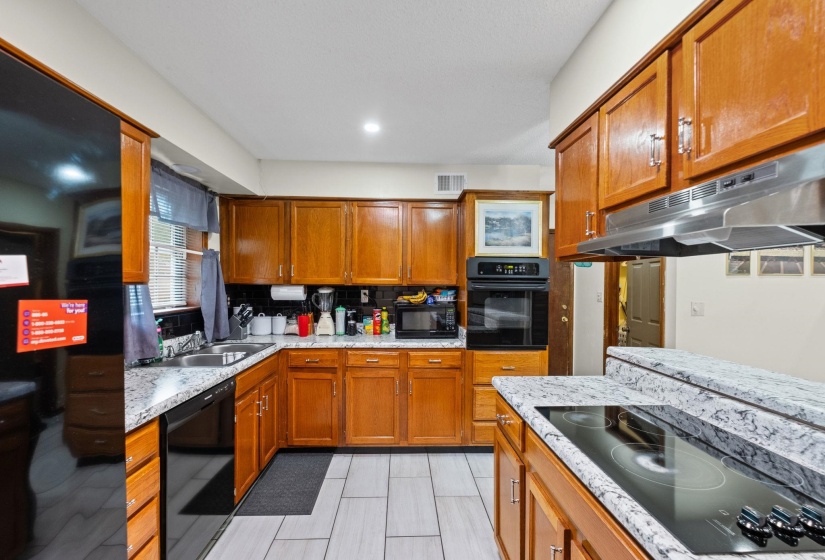 Kitchen featuring wood cabinetry, light-toned speckled countertops, tile flooring, a built-in oven, and a black cooktop