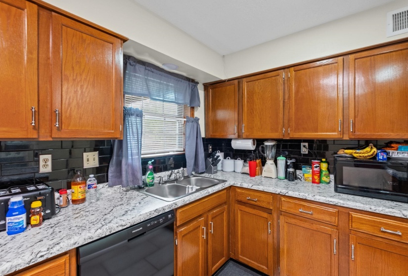 Kitchen featuring wood cabinetry with silver-tone hardware, a black subway tile backsplash, and light-toned mottled countertops