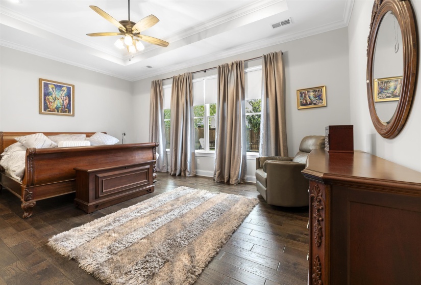 Spacious room featuring wood-finish flooring, a tray ceiling with a ceiling fan, and multiple windows with transoms