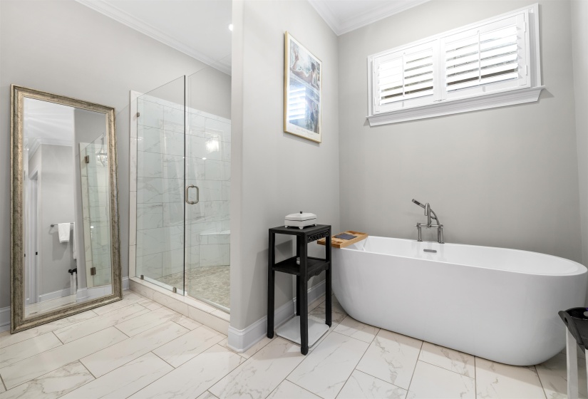 Freestanding soaking tub with floor-mounted faucet, glass-enclosed shower with tile surround and built-in bench, and plank-style tile flooring