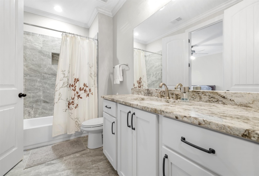 Bathroom featuring a double vanity with stone-finish countertop, white cabinetry with matte black hardware, and an integrated mirror