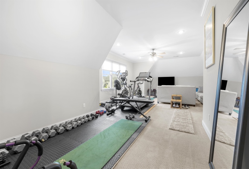 Spacious room featuring sloped ceilings, recessed lighting, and a ceiling fan