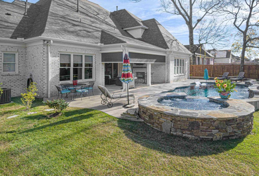 Expansive outdoor living area featuring a custom-shaped swimming pool with an integrated stone-clad spa