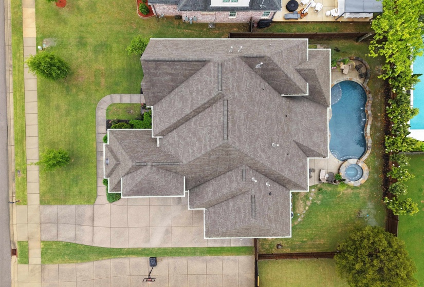 Expansive property featuring a multi-gabled roof, a large concrete driveway, a manicured lawn, a freeform swimming pool, and an integrated spa