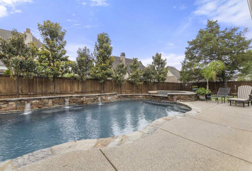 Resort-style backyard featuring a dark-bottom swimming pool with three water features, a built-in spa, flagstone coping, and a textured concrete patio