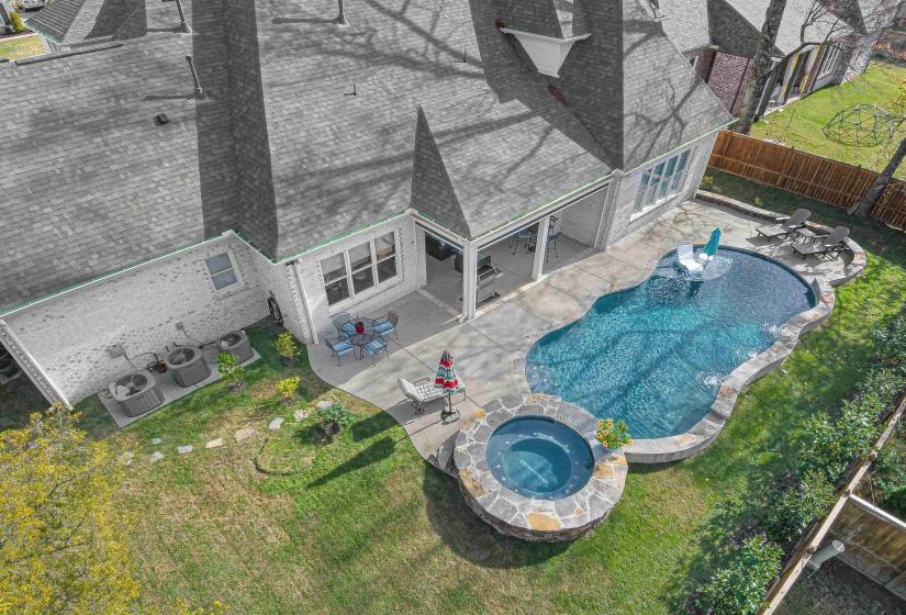 Resort-style backyard featuring a freeform swimming pool, integrated spa with stone surround, a covered patio, and a spacious concrete patio area