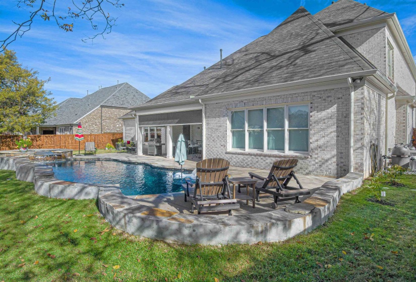 White brick exterior featuring a multi-level stone patio, an in-ground swimming pool, and a covered outdoor living area