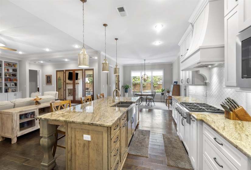 Gourmet kitchen featuring a large island with integrated sink, stone countertops, professional-grade range, white cabinetry, and herringbone tile backsplash