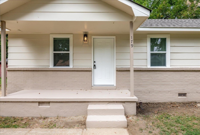 View of exterior entry with crawl space, a porch, brick siding, and a shingled roof