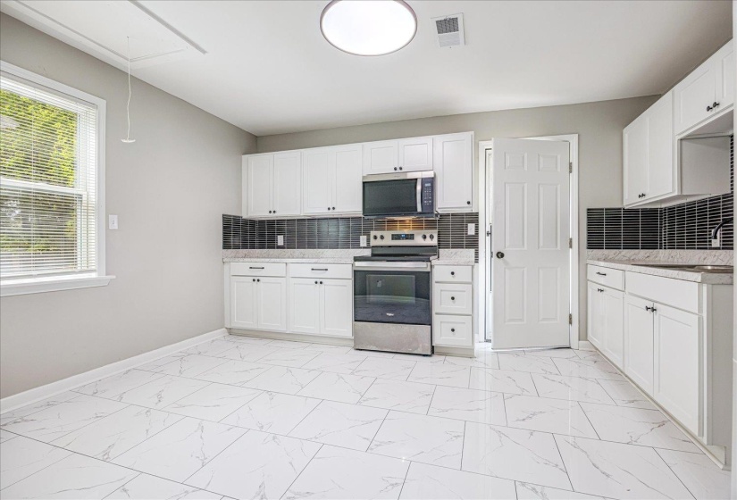Kitchen featuring backsplash, stainless steel appliances, white cabinetry, and light marble finish floors