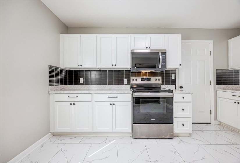 Kitchen featuring backsplash, appliances with stainless steel finishes, and white cabinetry