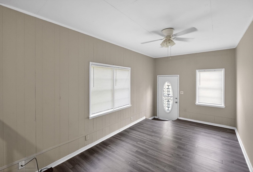Spacious room featuring dark wood-finish flooring, light tan paneled walls, and a white ceiling with a mounted fan