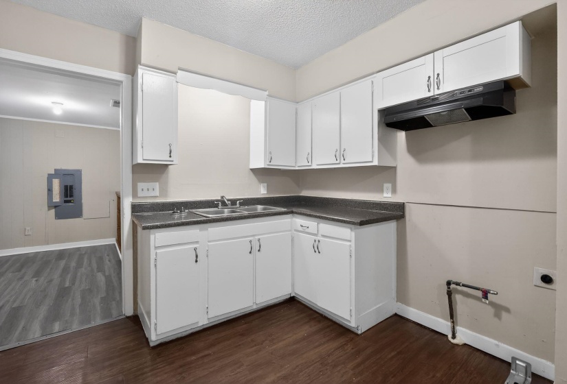 Kitchen featuring white cabinetry, a double basin sink, dark stone-finish countertops, a black range hood, and wood-finish flooring