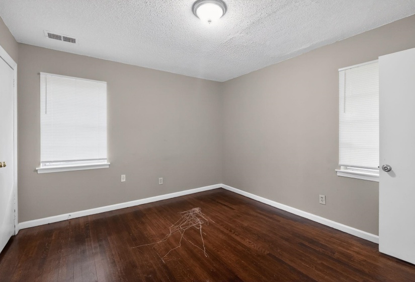 Spacious interior room with wood-finish flooring, neutral wall tones, and overhead lighting