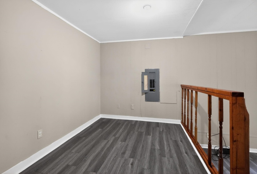 Interior room featuring wood-finish flooring, light tan wall panels, white baseboards, and white crown molding