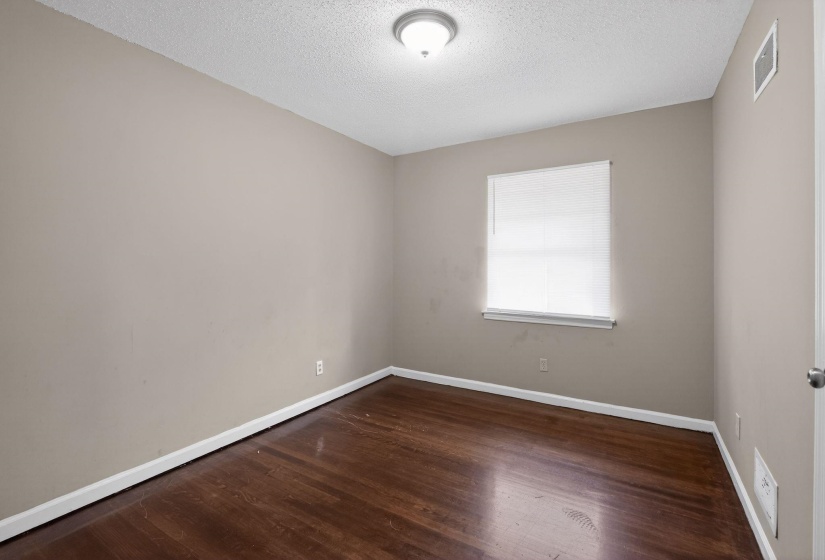Hardwood-finish flooring with white trim, neutral wall paint, and a textured ceiling