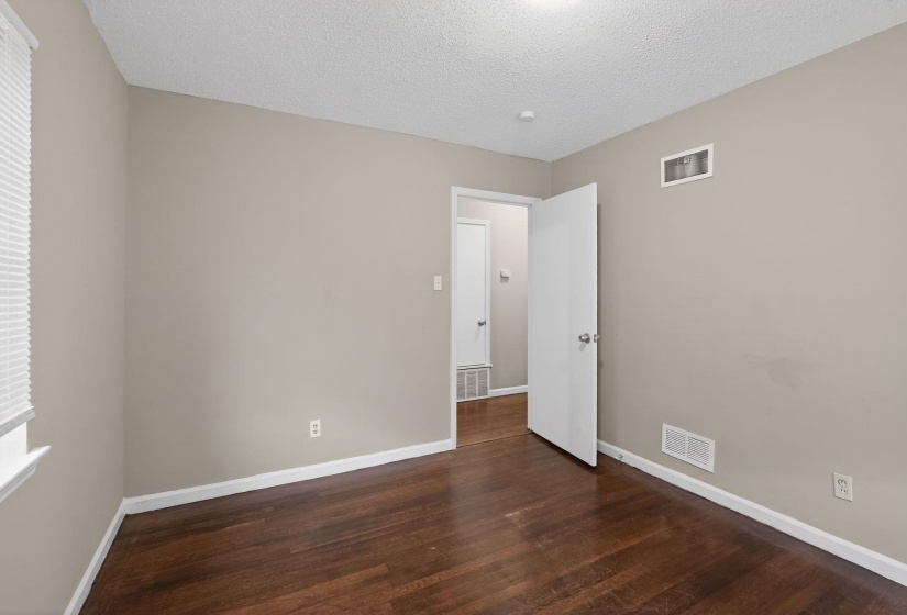 Interior room featuring rich wood-finish flooring, neutral-toned walls, white trim, and a window with blinds