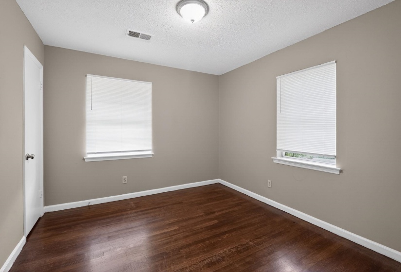 Room with wood-finish flooring, two windows with blinds, a white door, and a ceiling-mounted light fixture