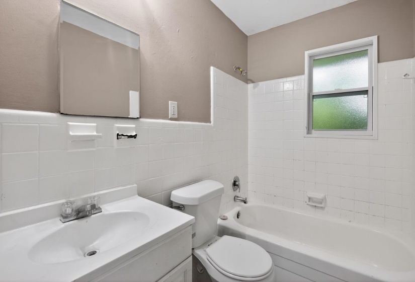 Bathroom featuring a white vanity with integrated sink, white tiled walls, a standard toilet, and a white bathtub with a shower fixture