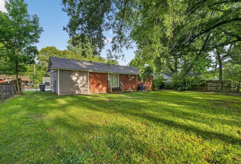 Expansive backyard featuring a lush green lawn, mature trees providing natural shade, and a privacy fence