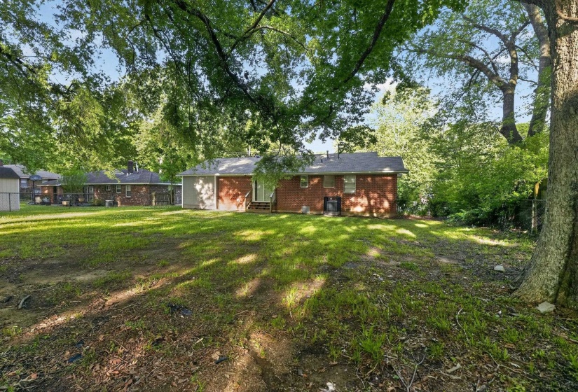 Spacious backyard featuring established trees, a brick exterior residence, and a modest rear deck