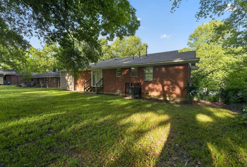 Expansive grassy backyard featuring a brick exterior, mature trees, a multi-tier wood deck, and sliding glass door access