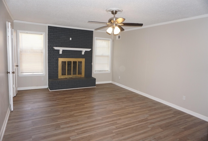 Living area featuring wood-finish flooring, a black brick fireplace with a white mantel, and multiple windows