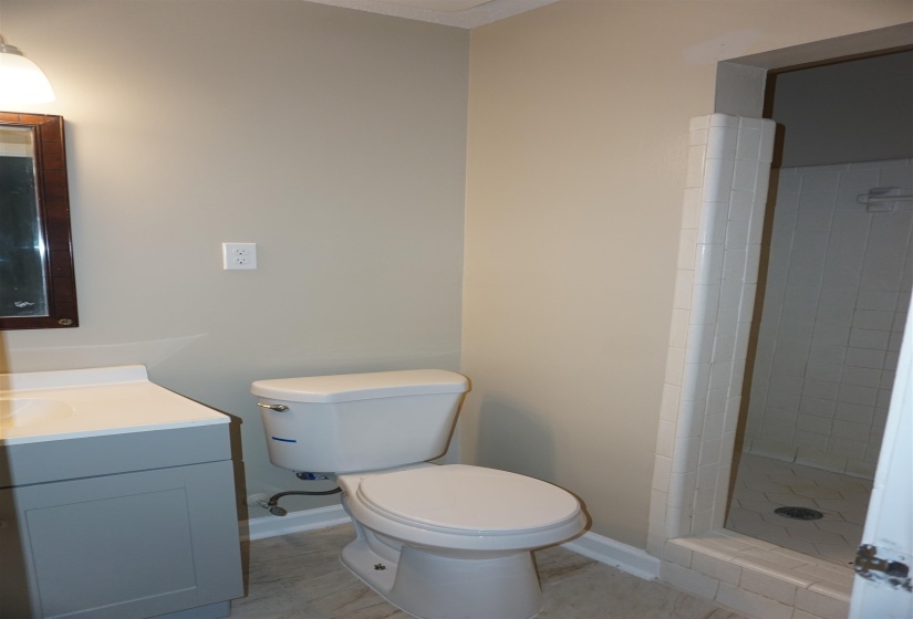 Bathroom featuring a white toilet, gray vanity with white countertop, and a tiled shower enclosure with a glass door