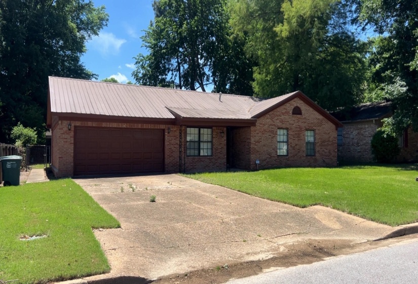 Brick exterior home with a brown metal roof, featuring an attached garage and a concrete driveway